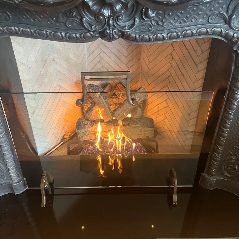 Gas log set burning behind a glass screen under an ornate carved black mantel
