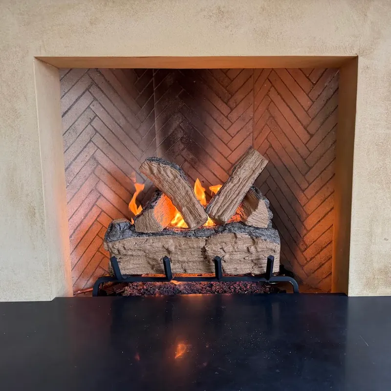 Gas log set burning in a herringbone brick firebox with a plaster surround